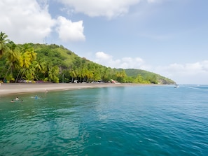 A beach with clear turquoise water, palm trees, and a hilly backdrop.