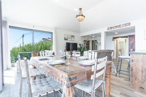 A spacious dining area with a large table set for a meal, a television in the background, and a view of the outdoors. - Casa Hui Nosso Refugio by Atlantic Holiday (Calheta)
