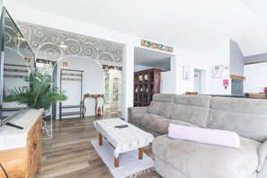 Ein Wohnzimmer mit grauem Sofa, einem kleinen Tisch mit Fernbedienung, einem Holzschrank und einem dekorativen Spiegel.