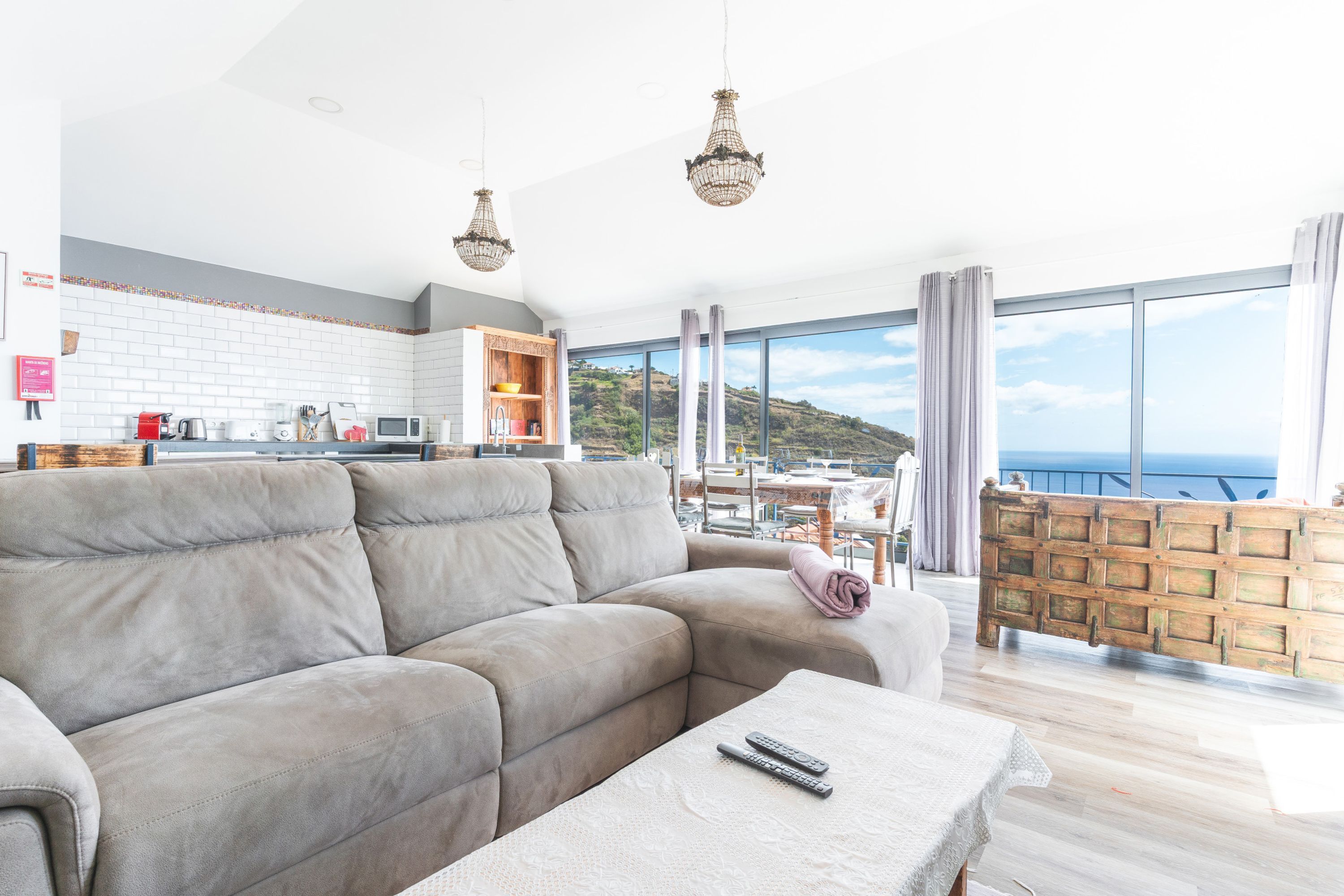 A modern living room with a grey sofa, a coffee table, and a view of the sea through large windows.
