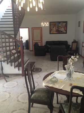 A living room with a staircase, a sofa, a dining table with chairs, and a painting on the wall.
