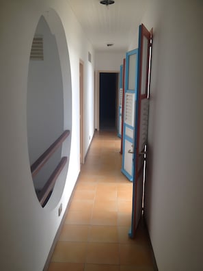 A corridor with a circular window, a door with a blue frame, and a tiled floor.
