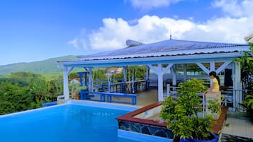 Un espace piscine doté d’un coin salon abrité, offrant une vue sur le paysage environnant et s’ouvrant sur un ciel dégagé.