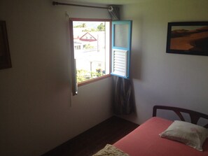Un dormitorio con cama, ventana con vista a edificios y un cuadro colgado en la pared.