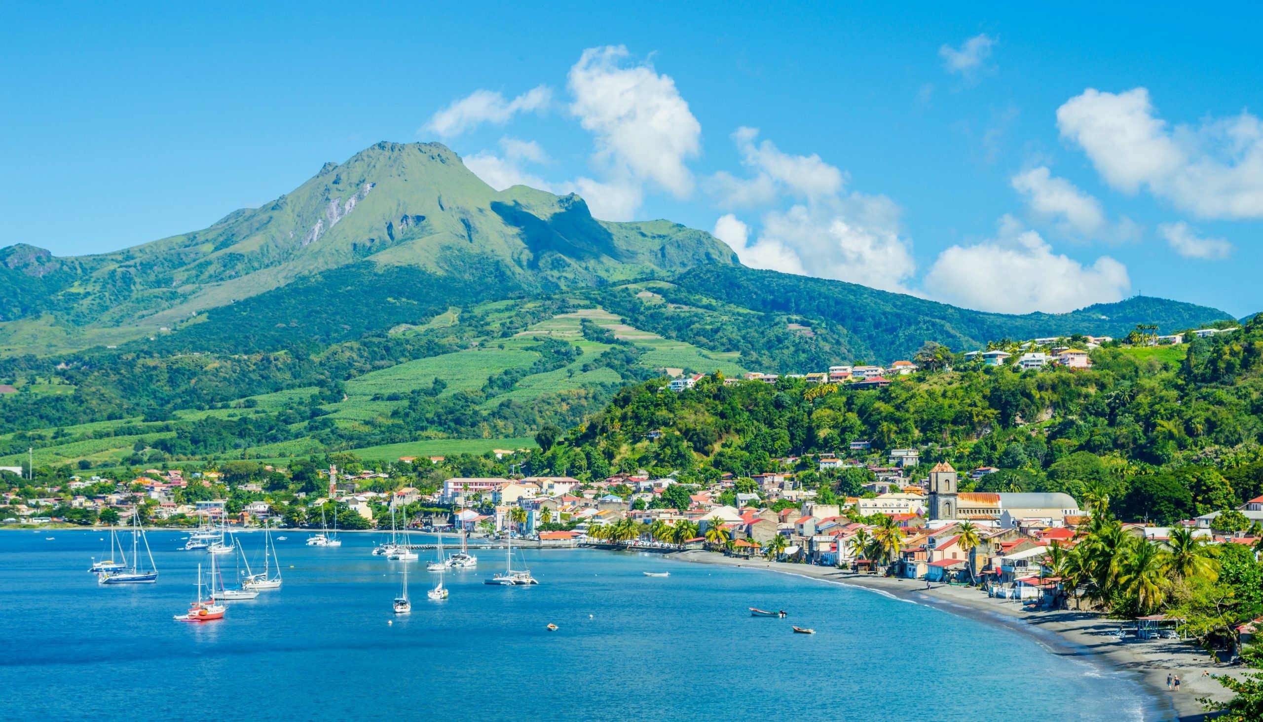 A coastal town with a mountain in the background, boats in the water, and buildings along the shore.