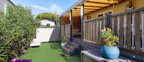 A covered outdoor area with a wooden deck, artificial grass, and a potted plant.