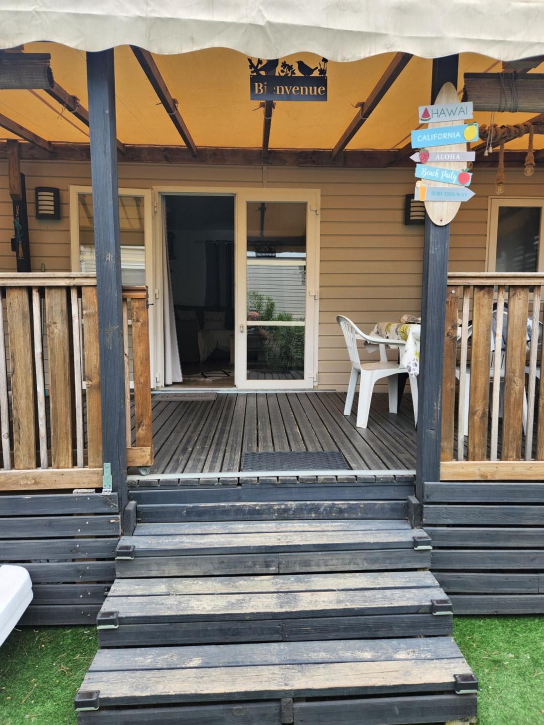 A wooden deck with a covered area, a signpost with destination names, and a table with chairs.