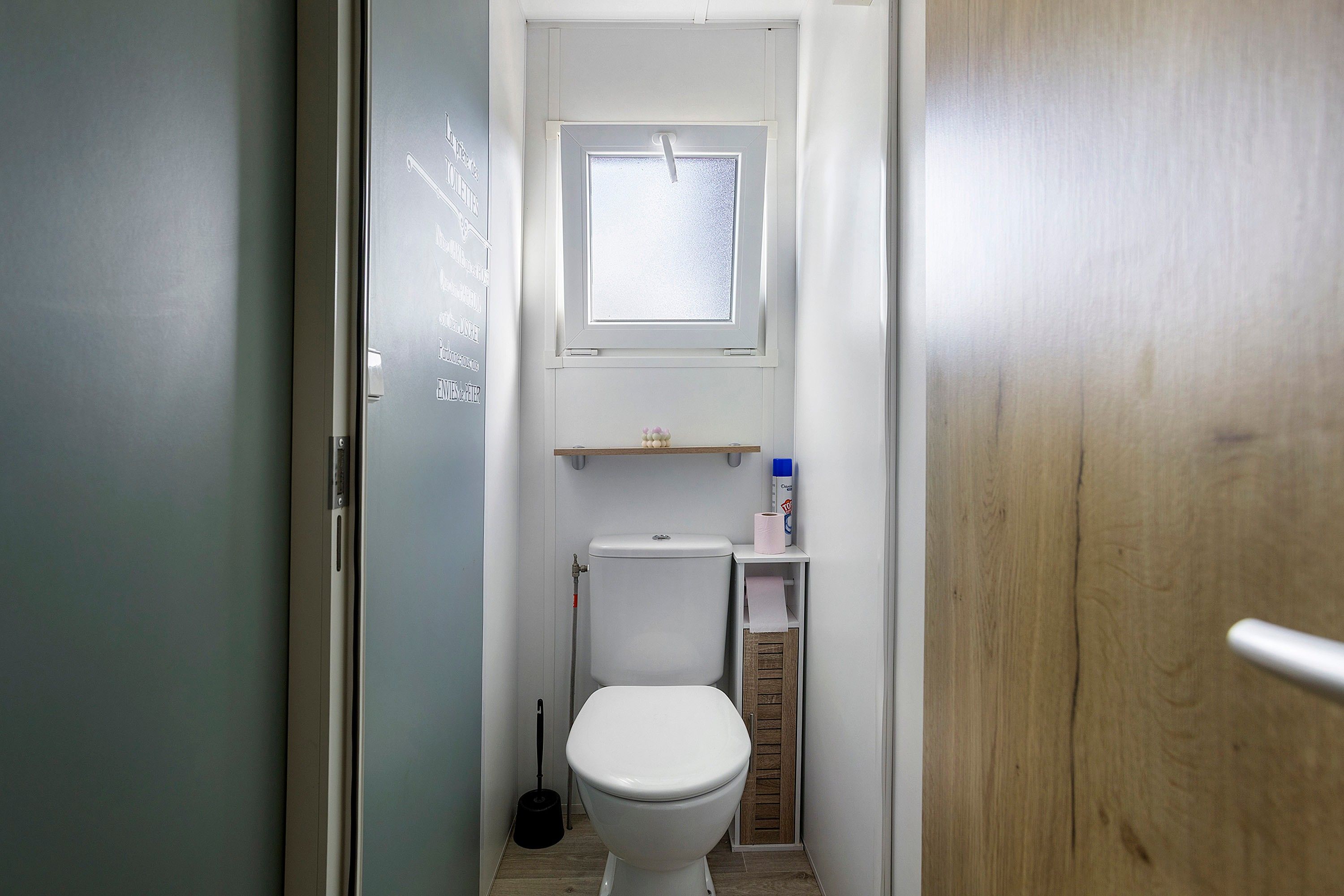 Un bagno stretto con il water, una finestra e uno scaffale con articoli da toilette.
