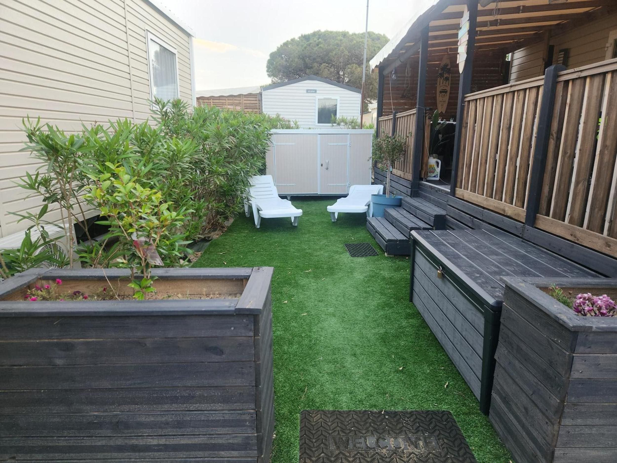 A backyard with artificial grass, two white lounge chairs, wooden planters, and a small shed.