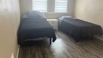 Une chambre avec deux lits simples, une table de chevet et une fenêtre avec des stores.