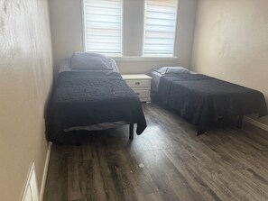 Un dormitorio con dos camas individuales, una mesita de noche y una ventana con persianas.