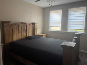 A bedroom with a wooden headboard, a bed with a dark bedspread, two bedside tables, and a window with blinds. - Terrific 4-bedroom house Southside With 2 sitting areas. (Abilene)
