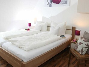 Ein Doppelbett mit weißer Bettwäsche, ein hölzernes Kopfteil und ein Nachttisch mit Lampe und Blume.