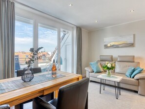 Ein modernes Wohnzimmer mit Essbereich, großen Fenstern, einer Sofagarnitur und einem Gemälde an der Wand.