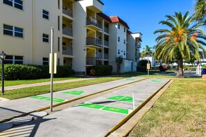 Un edificio residencial de varios pisos con balcones, un área de estacionamiento con espacios verdes y una palmera.