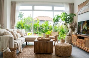 Ein Wohnzimmer mit Sofa, Couchtisch und Fernseher, mit Blick auf Grünfläche.