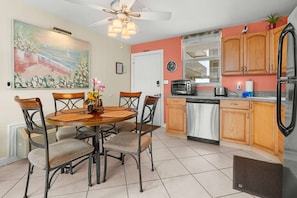A kitchen with wooden cabinets, a dining table with chairs, a ceiling fan, and a painting on the wall.