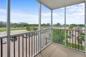 A balcony with a view of a parking lot, a road, and distant buildings.