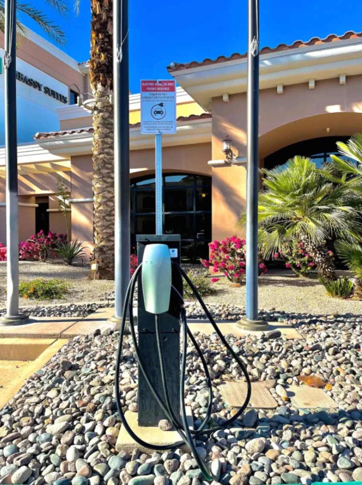 L’entrée d’un hôtel, avec un panneau indiquant un parking, une borne de recharge et un palmier.
