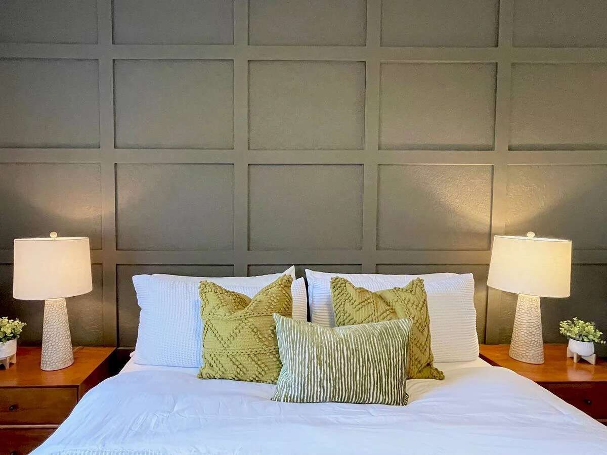 A neatly made bed with white bedding and multiple pillows, flanked by two bedside tables with lamps and small potted plants.