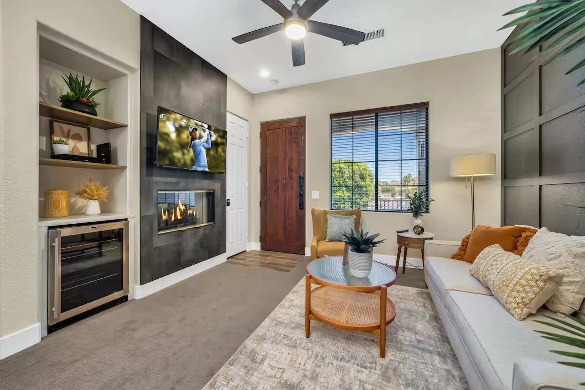 A modern living room with a fireplace, television, ceiling fan, and a sofa with cushions.