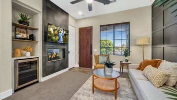 A modern living room with a fireplace, television, ceiling fan, and a sofa with cushions.