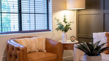 A cozy living room with a leather armchair, a side table with a lamp, a clock, and a potted plant.