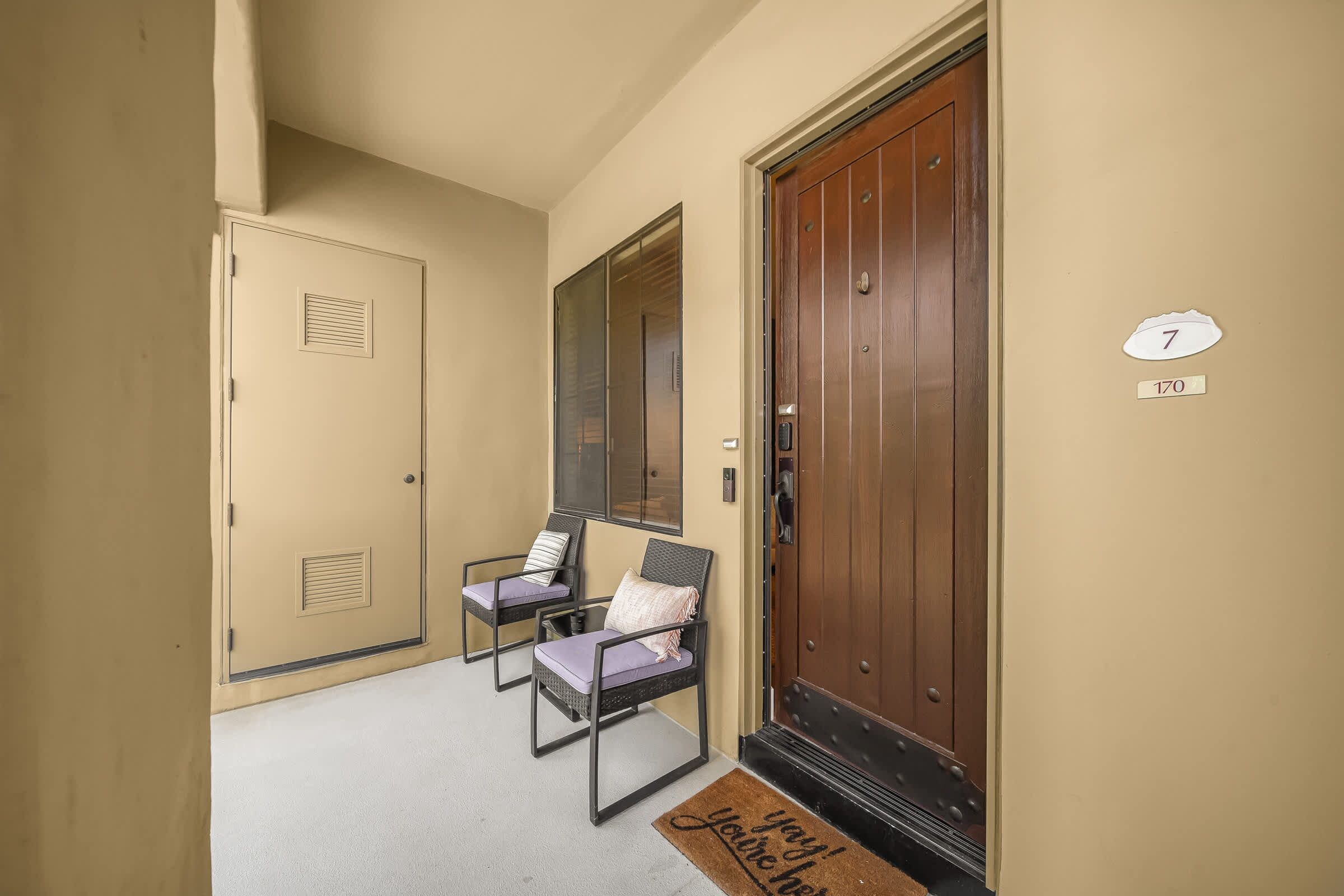 A hallway with a wooden door, a mirror, and two chairs with cushions.