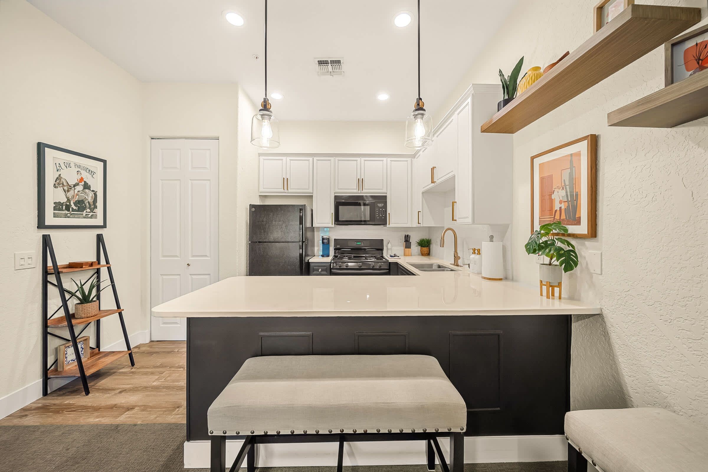 A modern kitchen with white cabinets, a black refrigerator, a stainless steel sink, and a central island with a bench.