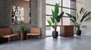 Een moderne lobby met een zithoek, grote ramen en potplanten.