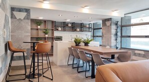 Een moderne keuken met een centraal eiland, barkrukken en een eettafel met stoelen.