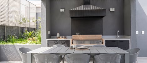 An outdoor kitchen with a grill, dining table, and chairs.