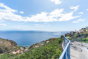Une vue sur la côte, avec un ciel dégagé, un balcon avec des chaises et une mer lointaine.