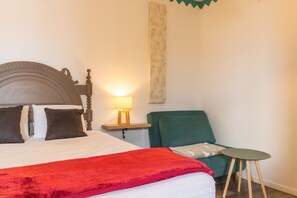 Ein Schlafzimmer mit einem Bett, einem Nachttisch mit Lampe, einem grünen Sessel und einem kleinen Tisch.