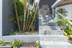 Un escalier en pierre mène à un mur de pierre, l’ensemble étant entouré de différentes plantes et d’une petite formation rocheuse.