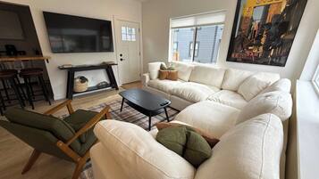 A modern living room with a sectional sofa, a small coffee table, and a TV mounted on the wall.
