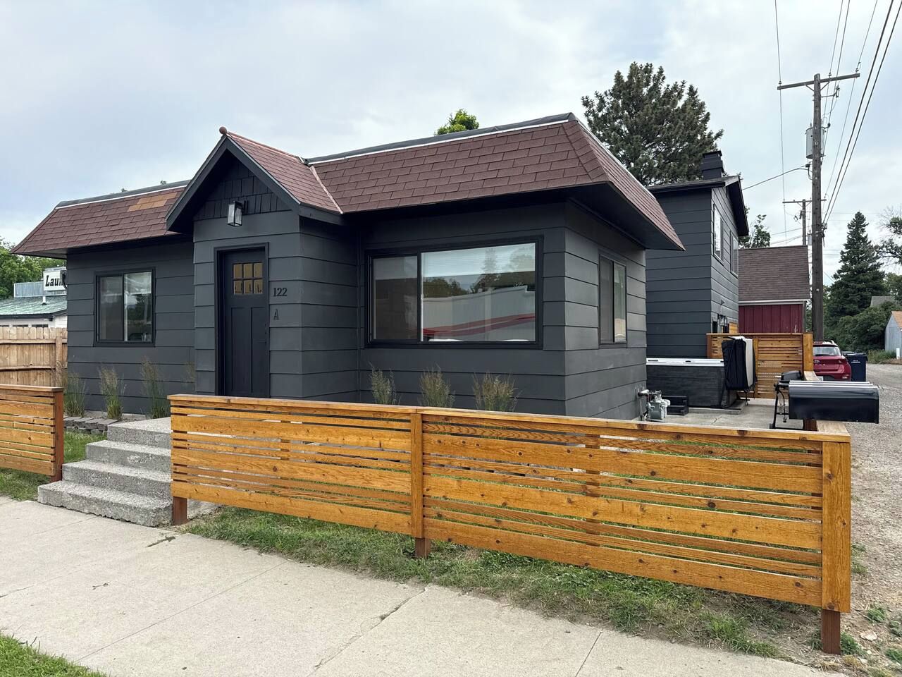 Ett modernt hus i två våningar med en mörk fasad, en veranda och ett trästaket.