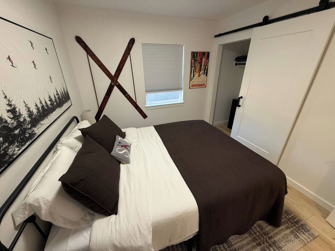 A bedroom with a bed, pillows, a window, a painting, and a door.