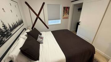 A bedroom with a bed, pillows, a window, a painting, and a door.