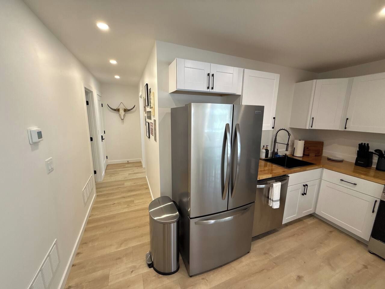 A modern kitchen with white cabinets, a stainless steel refrigerator, and a wooden countertop.