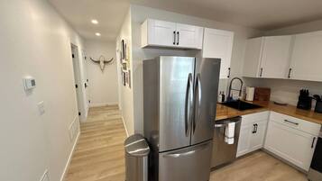 A modern kitchen with white cabinets, a stainless steel refrigerator, and a wooden countertop.