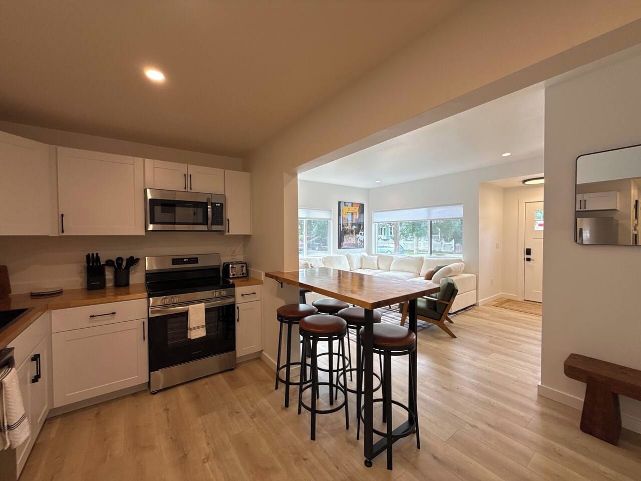 A modern kitchen with a central island, bar stools, and a dining area with a sofa.