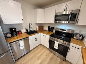 A modern kitchen with stainless steel appliances, white cabinetry, and a wooden countertop.