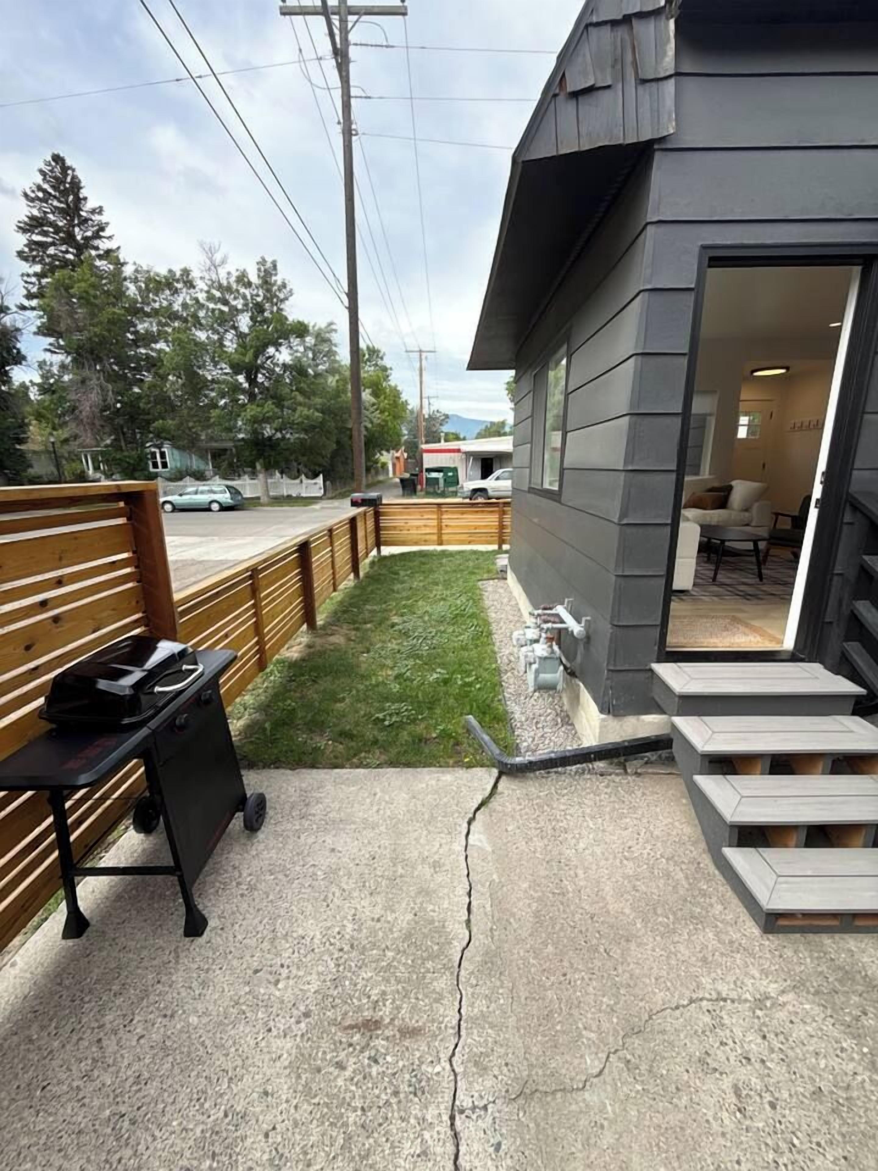 A residential property with a concrete driveway, a wooden fence, and a small lawn area.