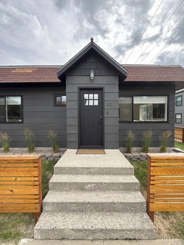 A modern building with a dark grey facade, a black door, and a number '122' on the wall.