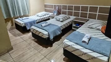 Habitación de hotel con tres camas, una ventana con cortinas, un equipo de aire acondicionado y piso de baldosas.