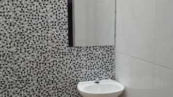 Ein Badezimmer mit einem weißen Waschbecken, einem Spiegel und Wandfliesen mit Muster.