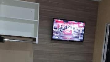 Una habitación compacta con una televisión montada en la pared, un refrigerador pequeño y un armario blanco.