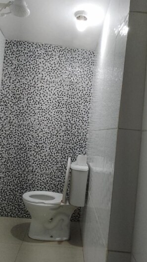 Un baño con inodoro, ducha y pared con azulejos.