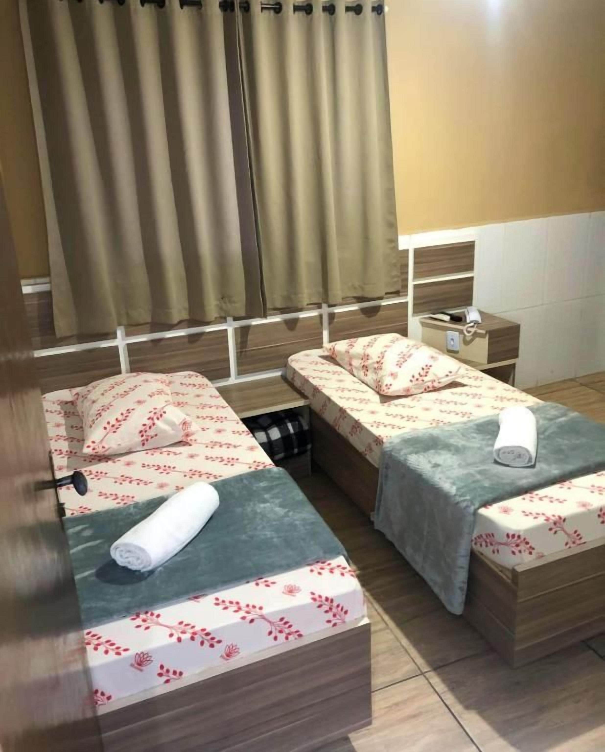 A hotel room with two beds, a nightstand, and a window with curtains.